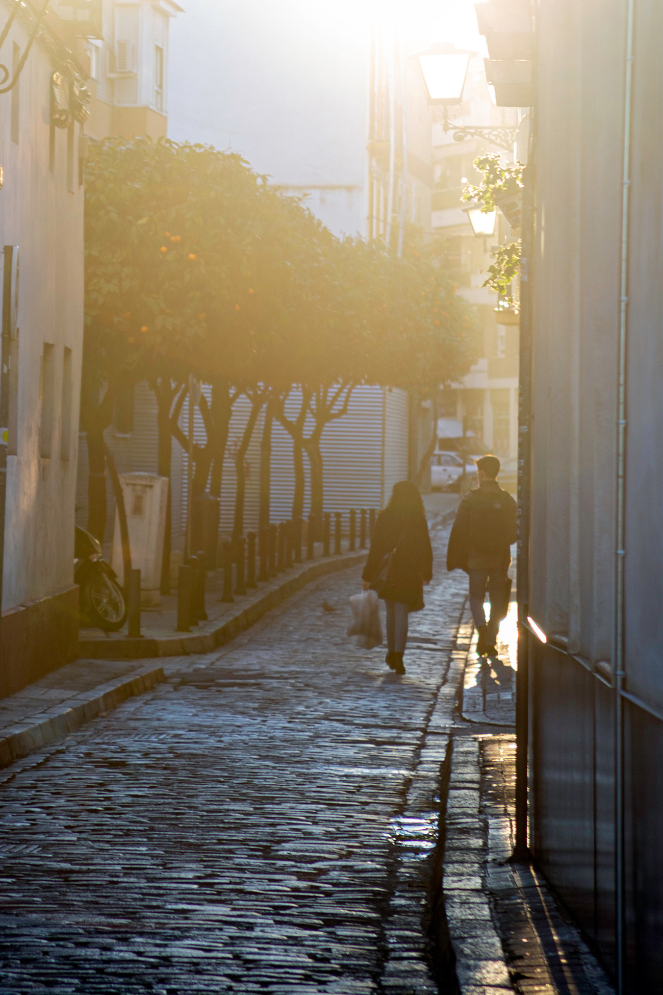 Two people walking down a narrow cobbled street in Seville in evening light