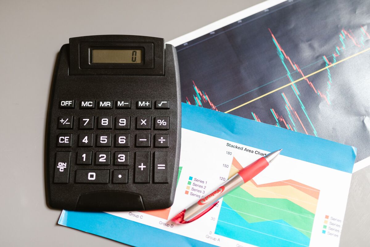 Black calculator beside printed stock and stacked area charts with a red pen on a desk