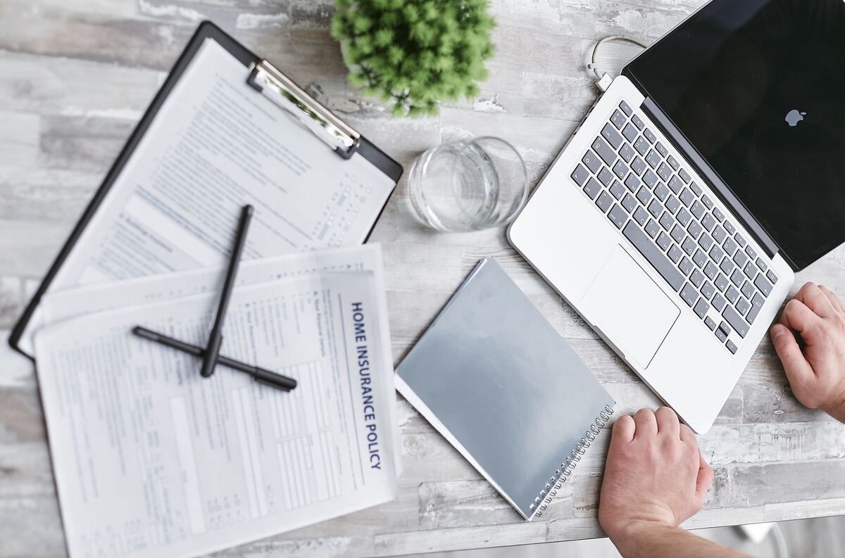 Overhead view of home insurance policy paperwork on a clipboard beside a laptop and notebook on a desk