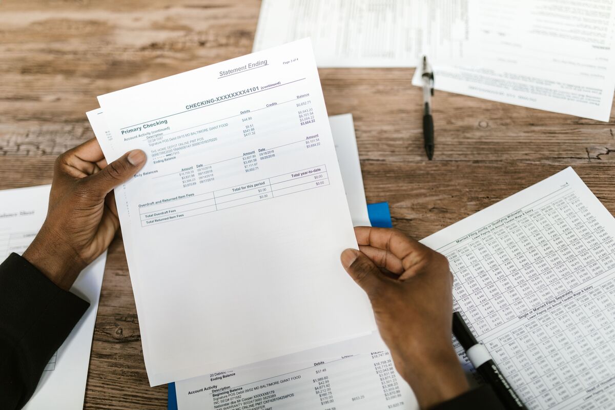 Hands holding a printed financial statement over a wooden desk scattered with reports and a pen