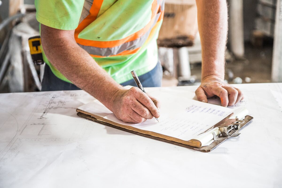 Construction worker in a hi-vis vest handwriting a job estimate on a clipboard over blueprints at a worksite