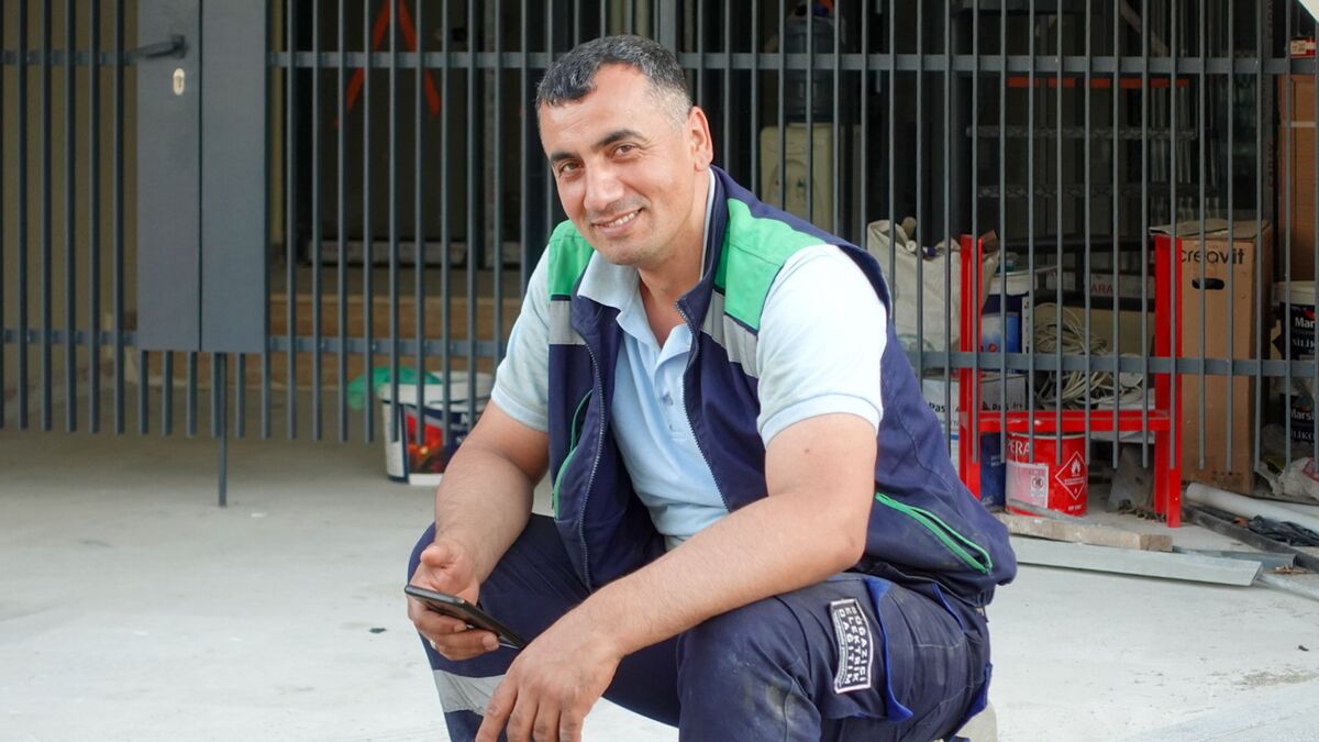 Smiling contractor in a work vest crouching at a building site with a smartphone in hand