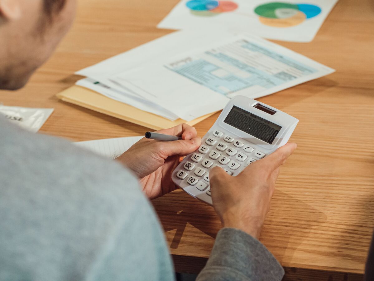 Person holding a calculator and pen while reviewing tax forms and financial charts on a wooden desk