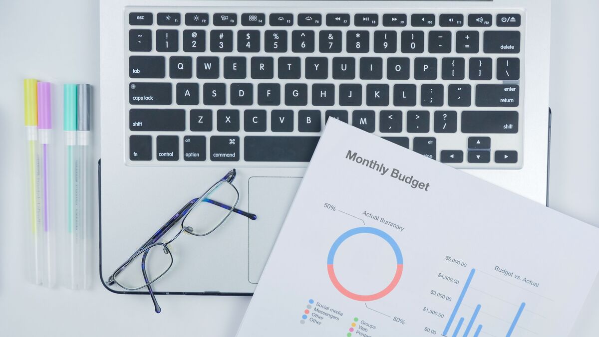 Monthly budget report with pie and bar charts beside eyeglasses and pens resting on a laptop keyboard