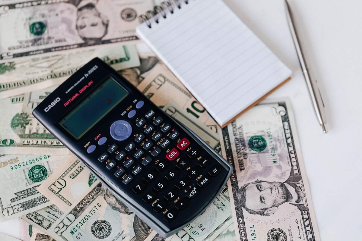 Calculator, blank notepad and pen resting on a spread of US dollar bills for budgeting and cash flow planning