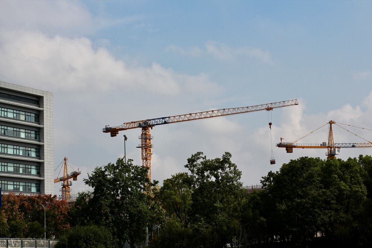 Tower cranes rising over a half-built modern building against a blue sky, signaling construction growth