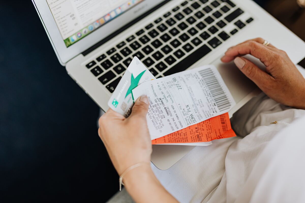 Person holding paper receipts and a bank card while reviewing finances on a laptop at a desk