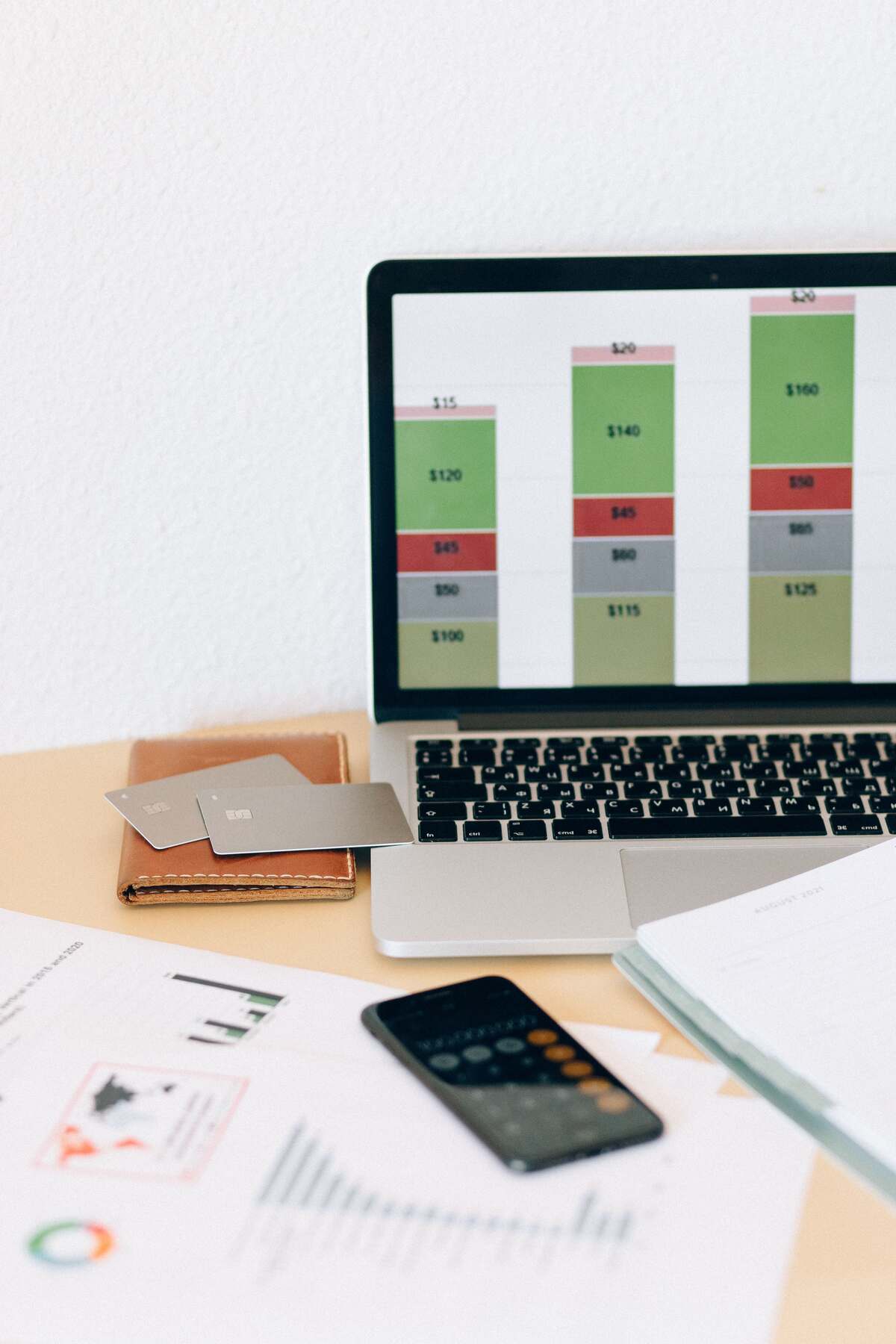 Laptop showing a colorful financial bar chart beside printed reports, a phone and cards on a desk