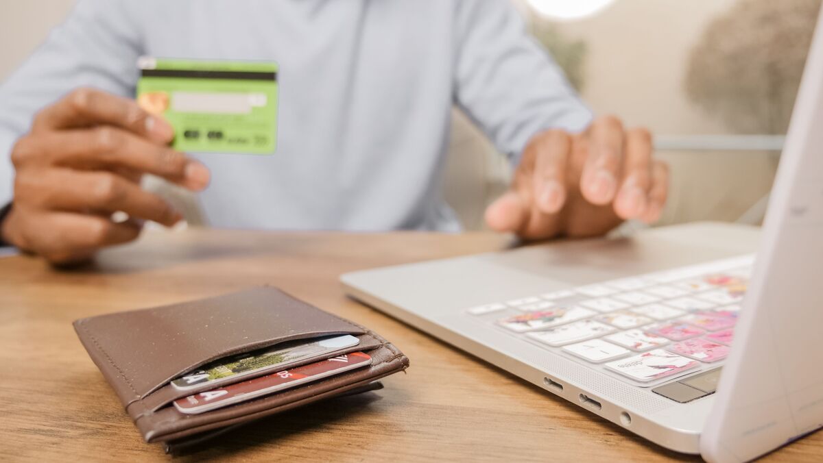Person at a desk holding a credit card while typing on a laptop, with a wallet of bank cards nearby