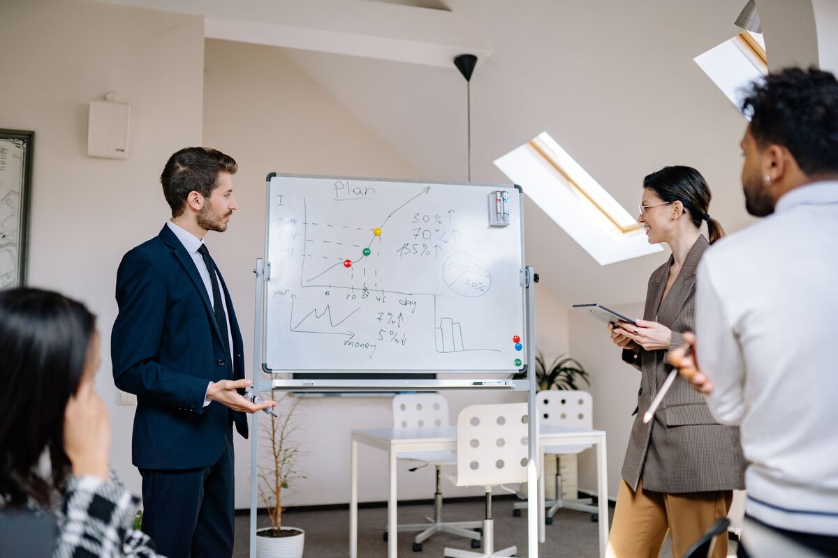 Business team reviewing a growth plan chart with numbers and percentages on an office whiteboard