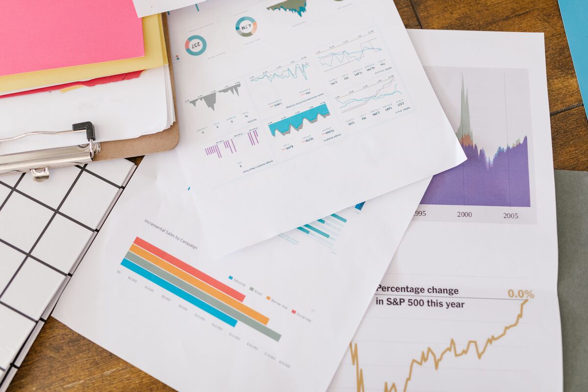 Printed financial reports with colorful bar charts and line graphs spread across a wooden desk beside a clipboard