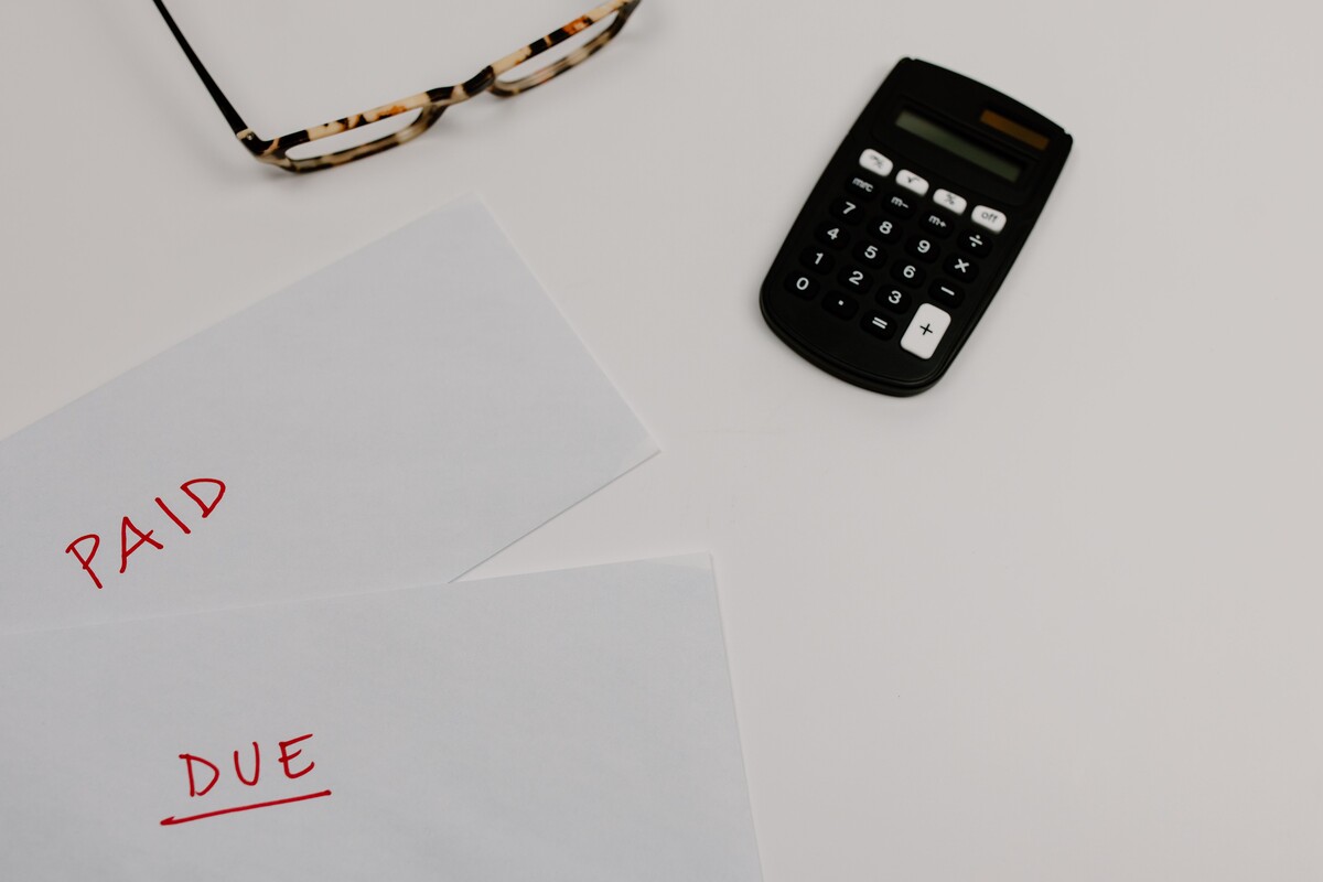 Envelopes marked Paid and Due in red beside a calculator and reading glasses on a white desk
