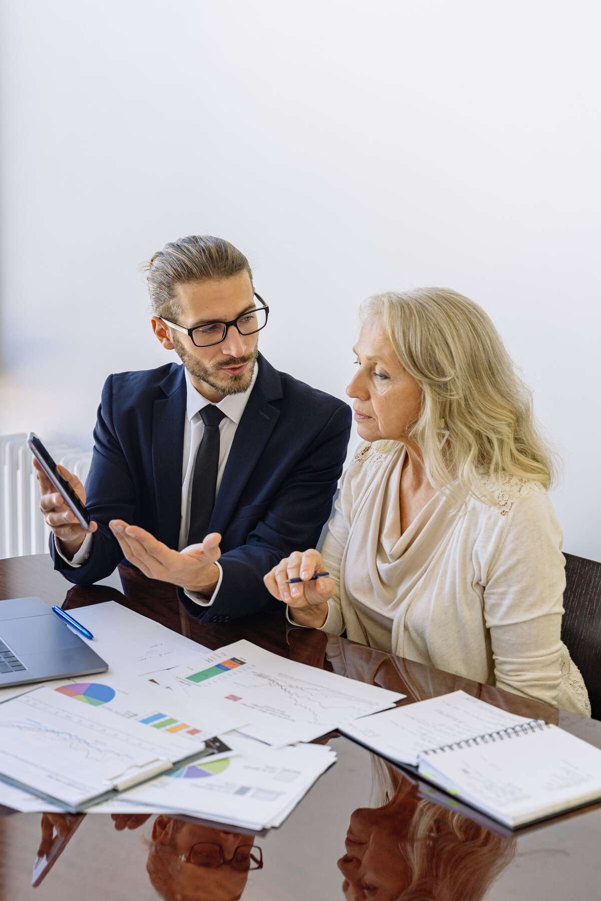 Advisor in a suit reviewing financial charts and documents with a client across an office table