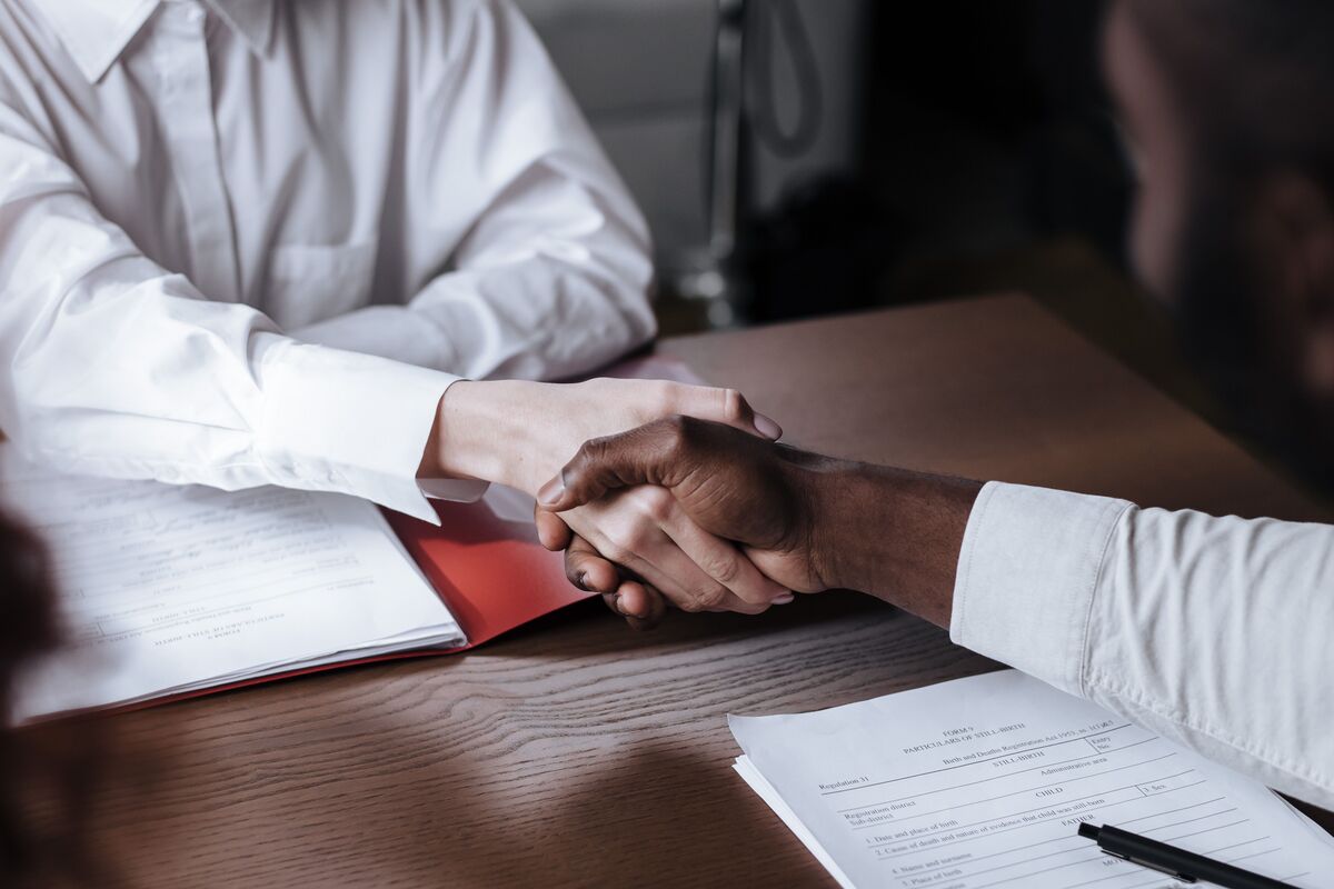 Two professionals shaking hands across a desk over signed paperwork, sealing a business deal