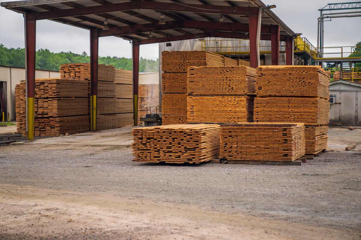 Stacks of fresh-cut lumber planks on pallets at an outdoor sawmill yard, ready for sale and pricing