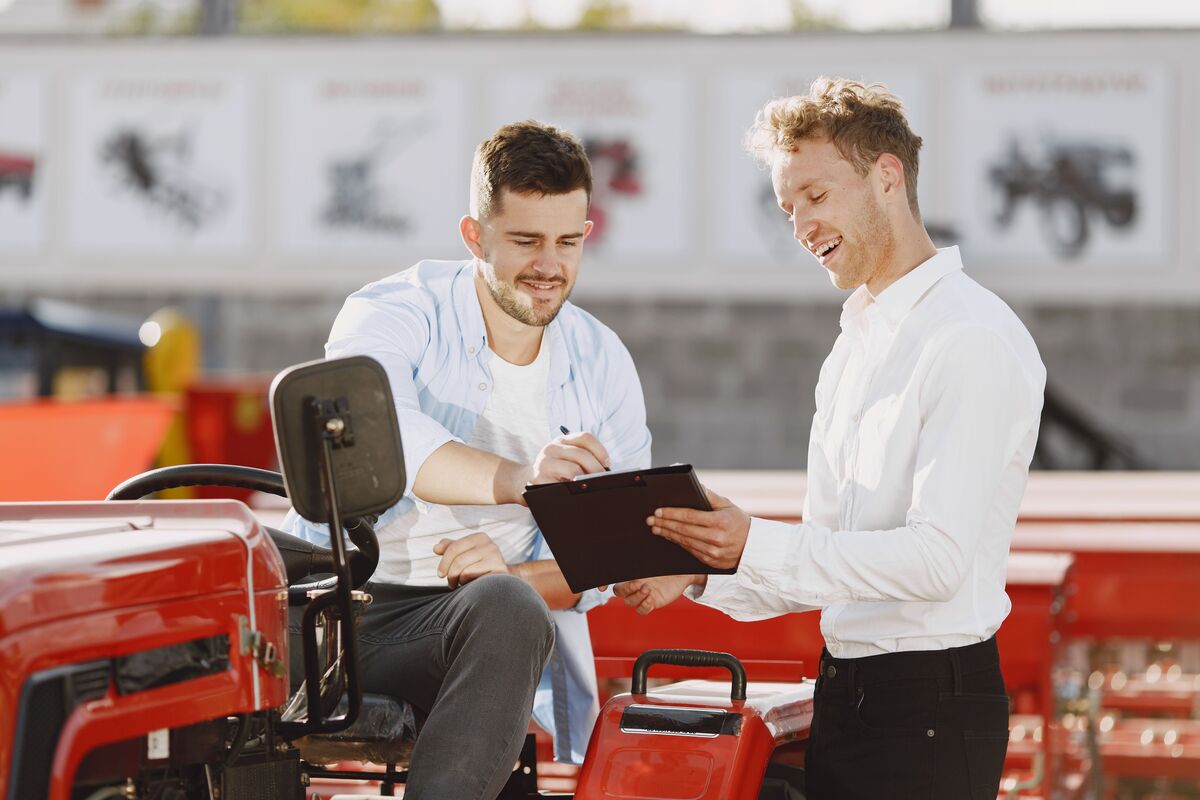 Contractor in a white shirt reviewing clipboard paperwork with a client beside red equipment outdoors