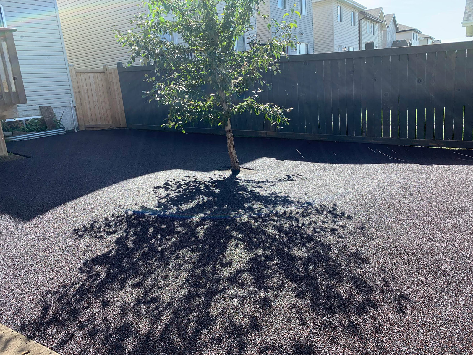 Outdoor residential patio space with dark rubber paving coating around trees