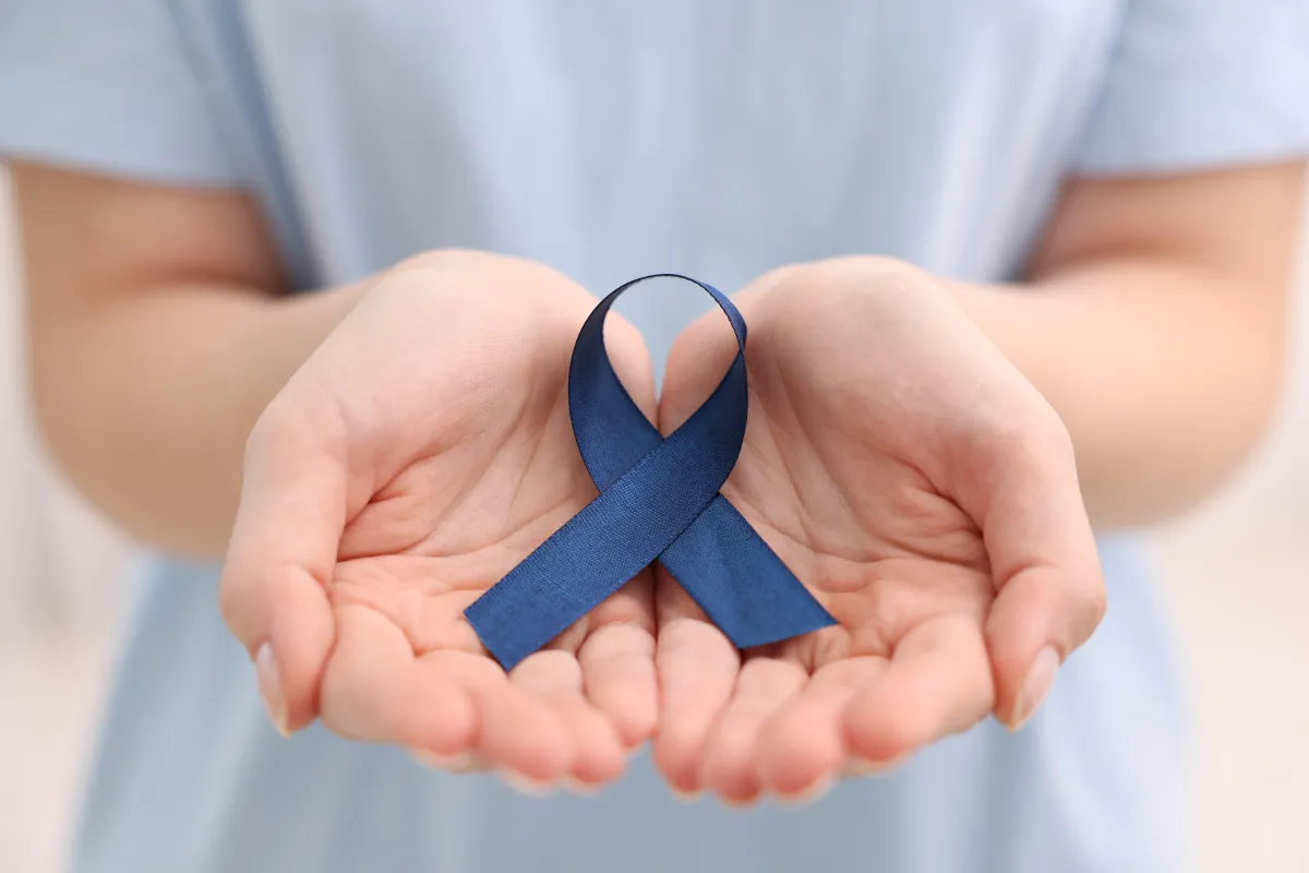 Woman with dark blue ribbon on light background, symbolising support for cancer