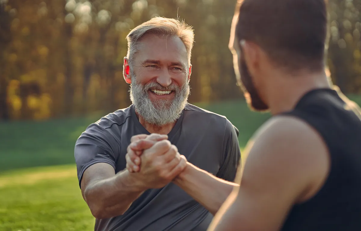 Healthy older man shaking hands with a younger man outdoors — men's health, fitness, and vitality support.