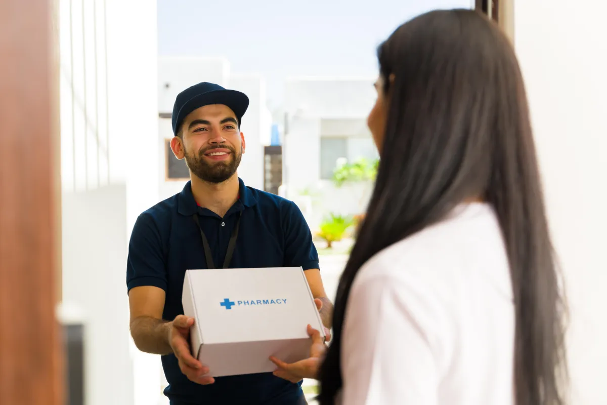 Smiling courier delivering a pharmacy box to a customer’s home — fast and discreet prescription delivery service.