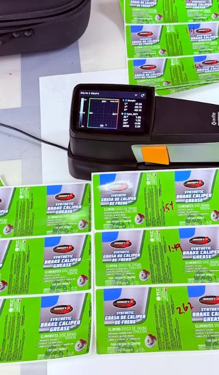 Professional woman reviewing generic label artwork on a computer monitor with printed proofs and color references in an in-house prepress workspace