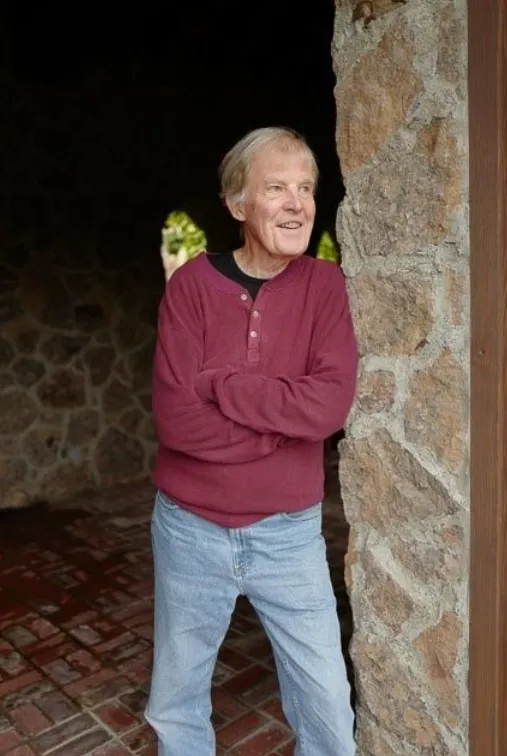 Bob Frissell seated in a warm study, medium shot 1:1 portrait format, natural window light, books and plants blurred in background, relaxed pose, candid photorealistic moment conveying approachability and lived experience.