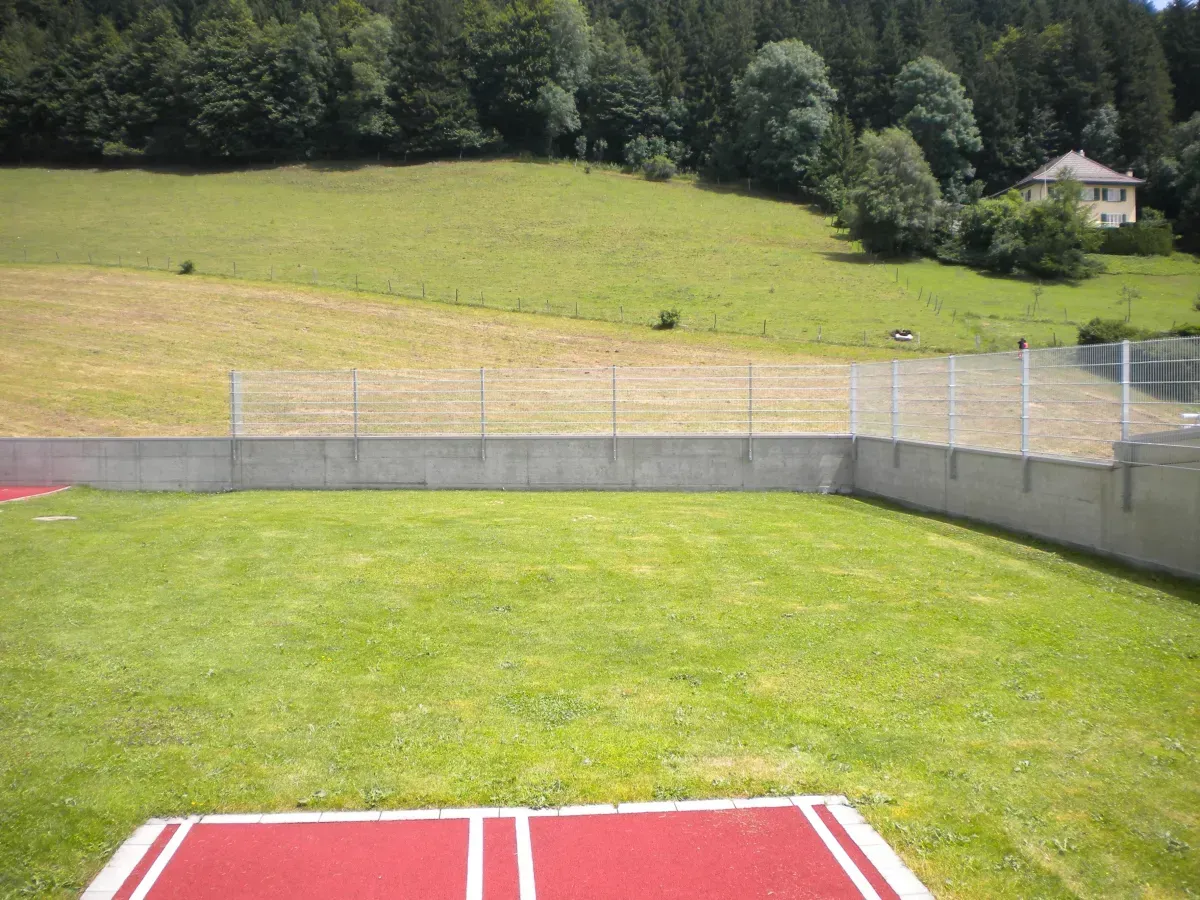 Espace extérieur avec gazon et clôture en acier, entouré de verdure, illustrant une solution de sécurité pour terrains sportives ou résidences.