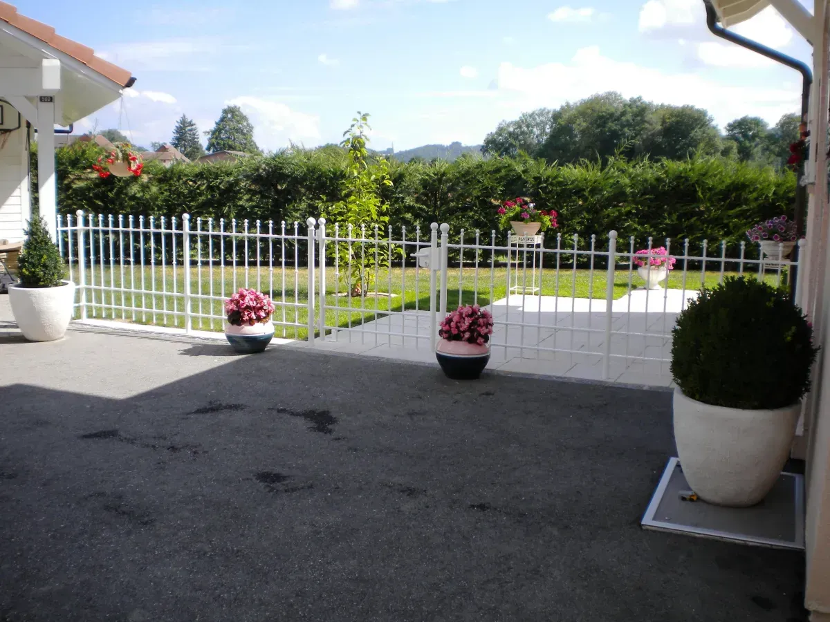 Clôture en fer forgé blanche entourant un jardin, pots de fleurs colorés, espace extérieur soigné, mettant en valeur le savoir-faire de Ludic Clotures.