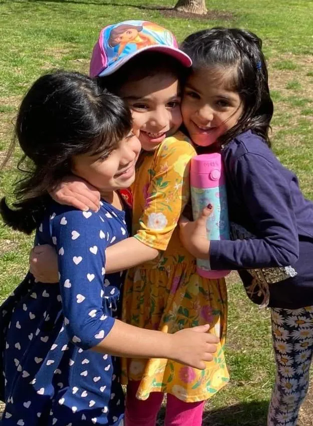 picture of three preschool girls outside. They are hugging.