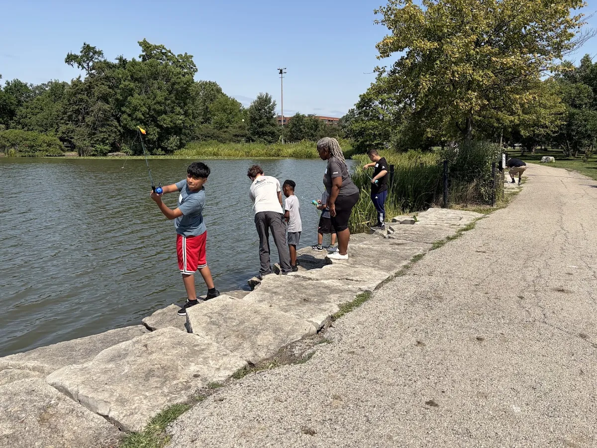 Children and adults fishing beside the lake at a MAF Humboldt Park outing.