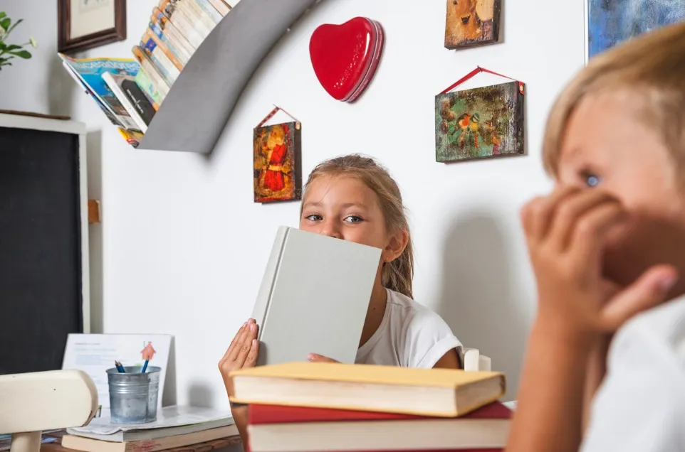  A smiling female tutor and a young girl work together at a desk in a classroom. The girl is filling out a colorful graphic organizer with a pencil while the tutor observes supportively