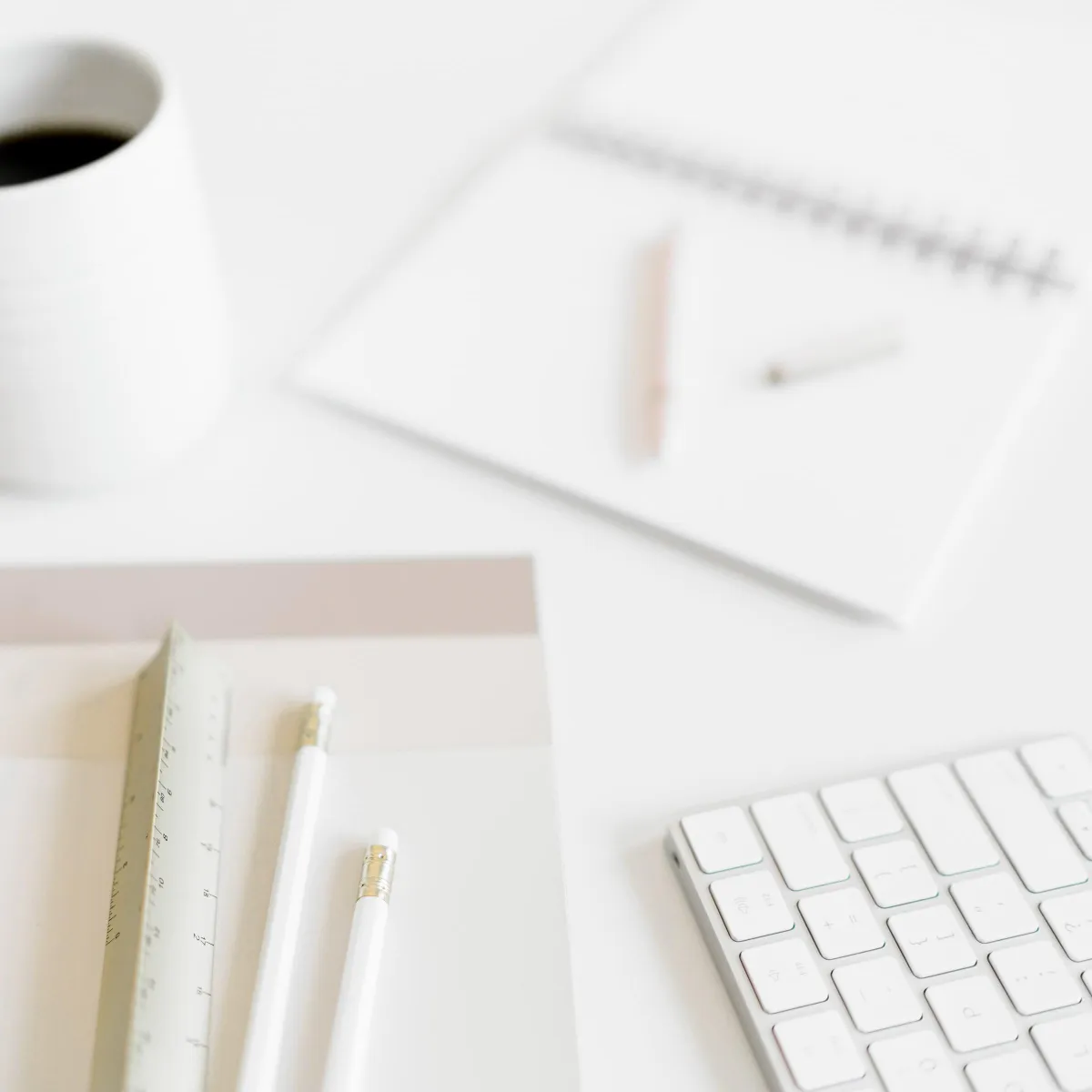 A notebook keyboard, coffee cup, and pencils on a white tabletop
