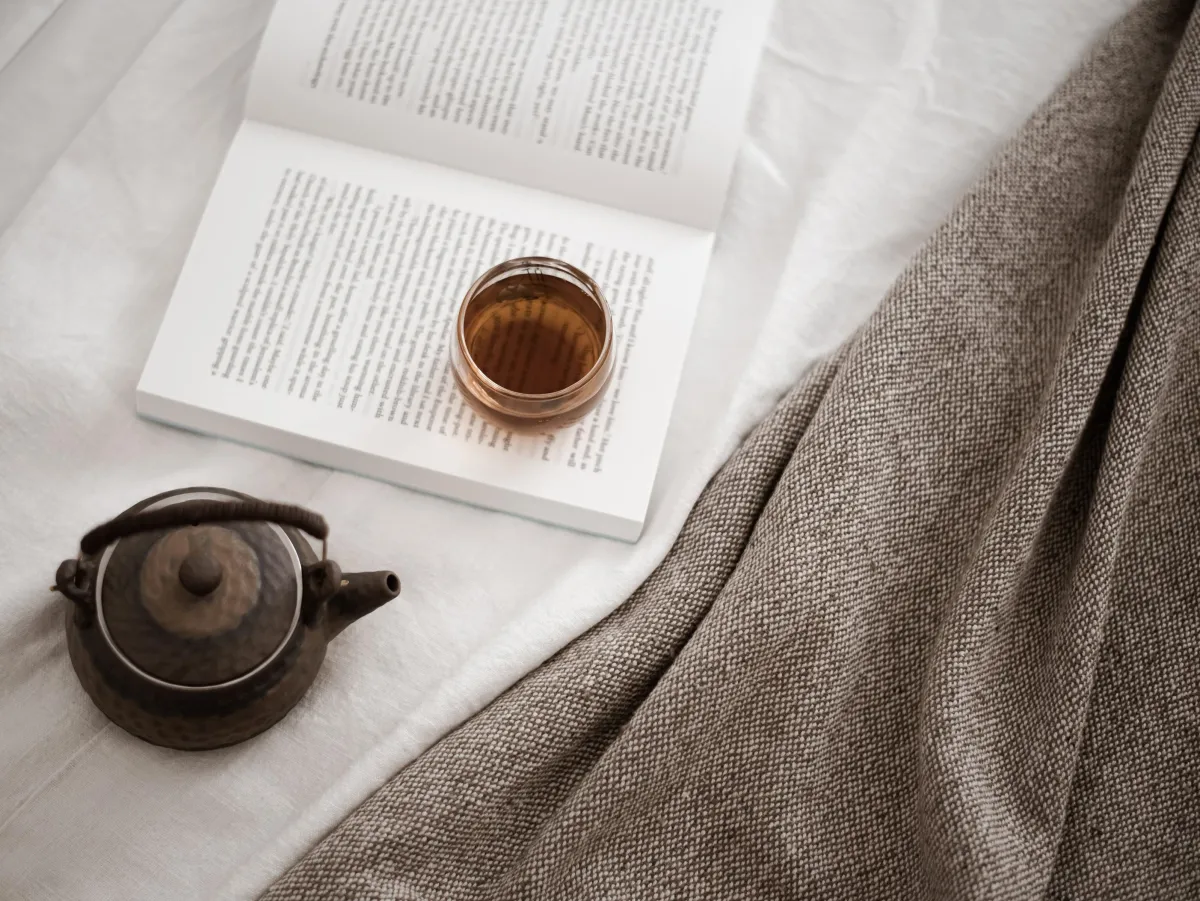 Open book on white and tan fabric with a cup of tea and teapot.