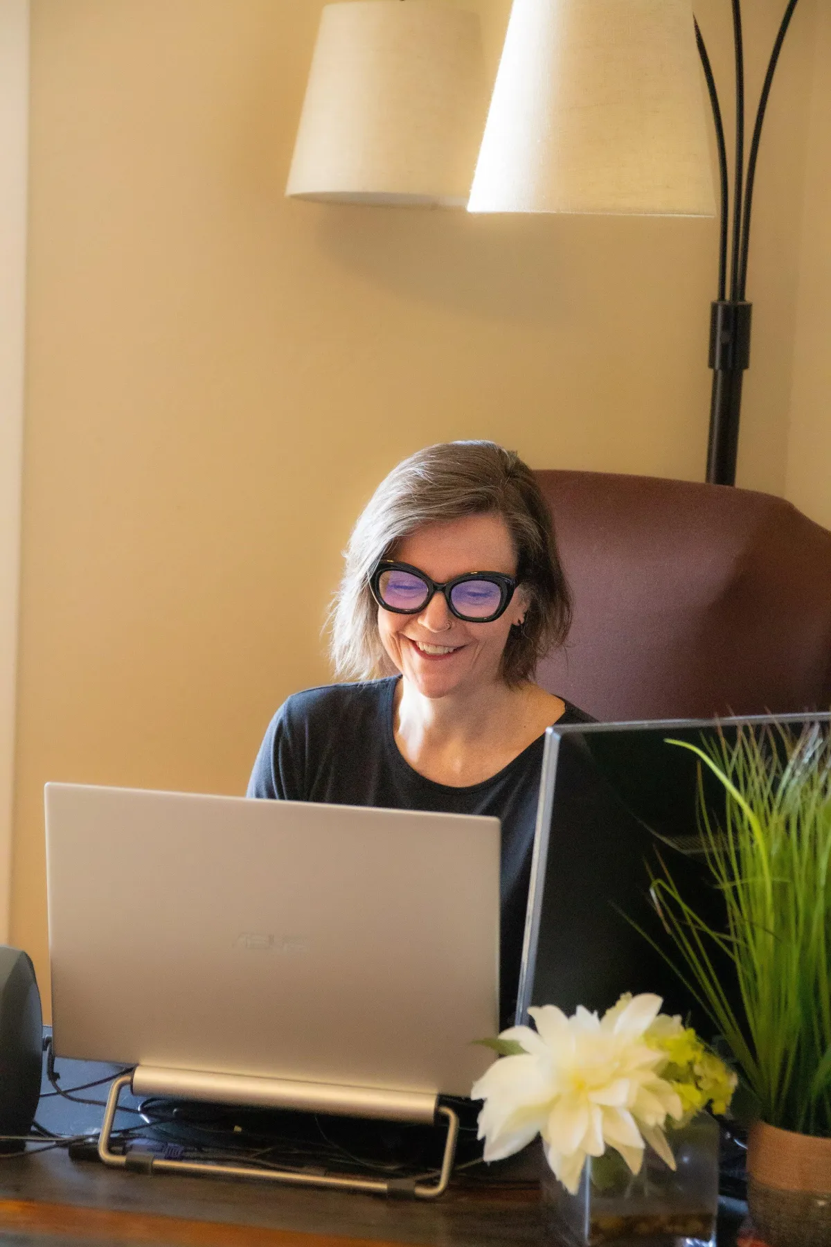 Book coach Maurene Janiece sitting at desk smiling facing laptop talking to a client.