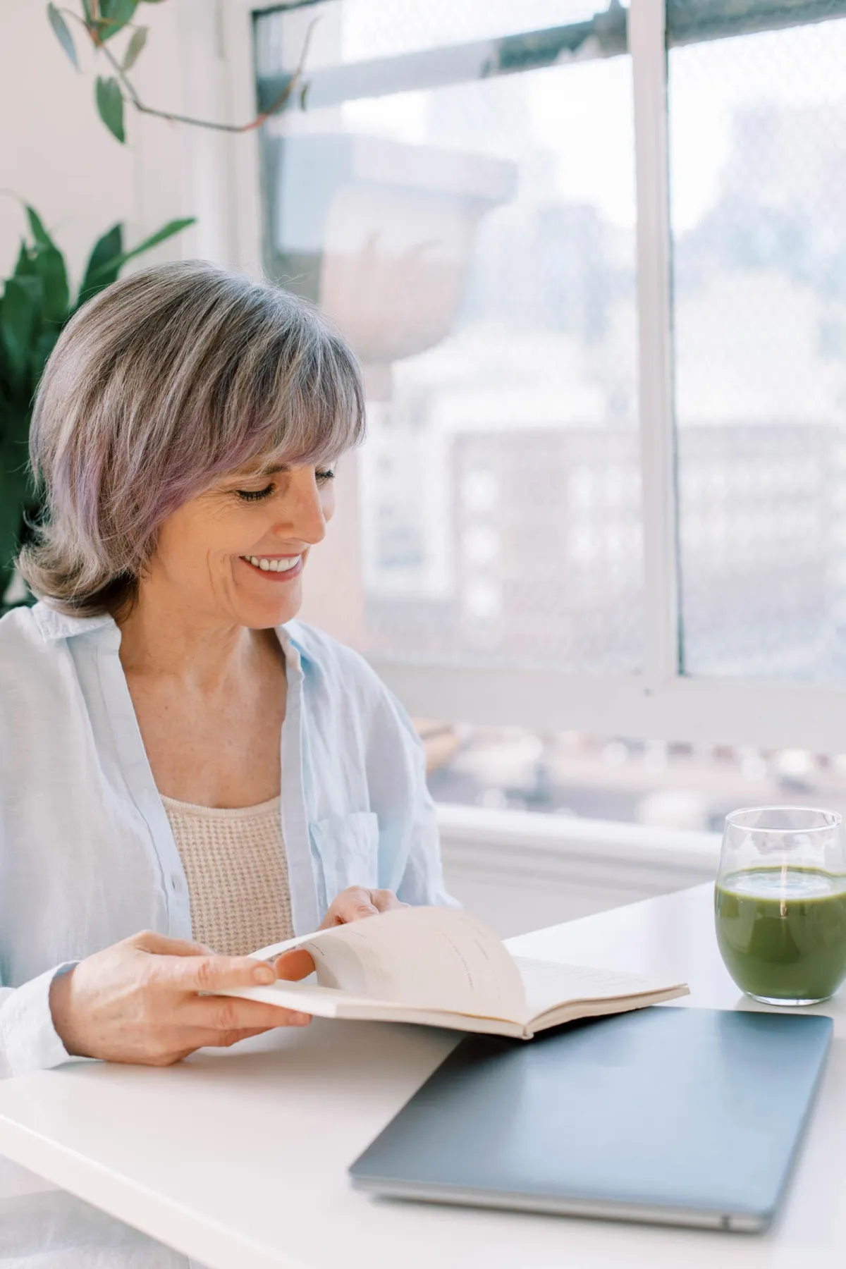 Mature woman at a table thumbing through a notebook and smiling.