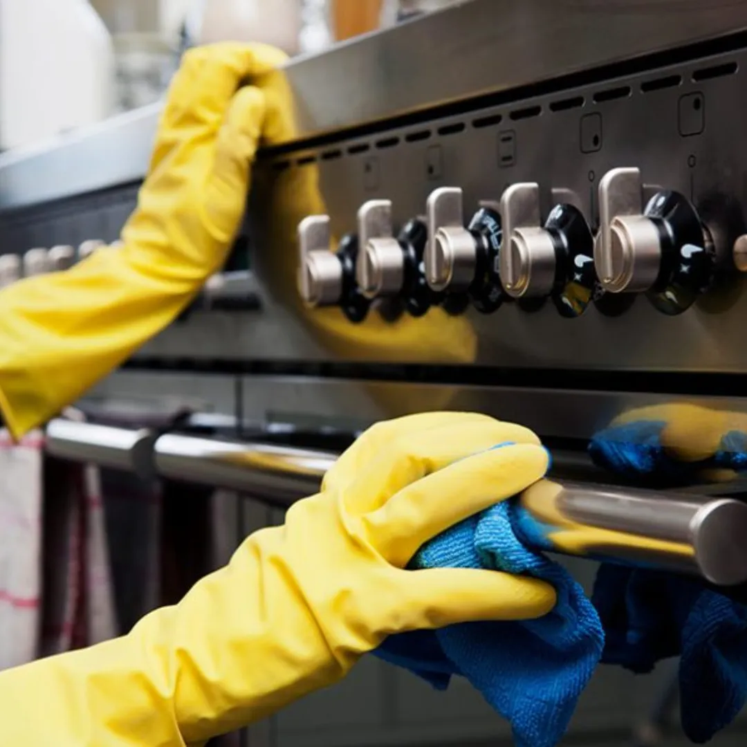 Cleaner scrubbing kitchen stovetop with yellow gloves during deep house cleaning