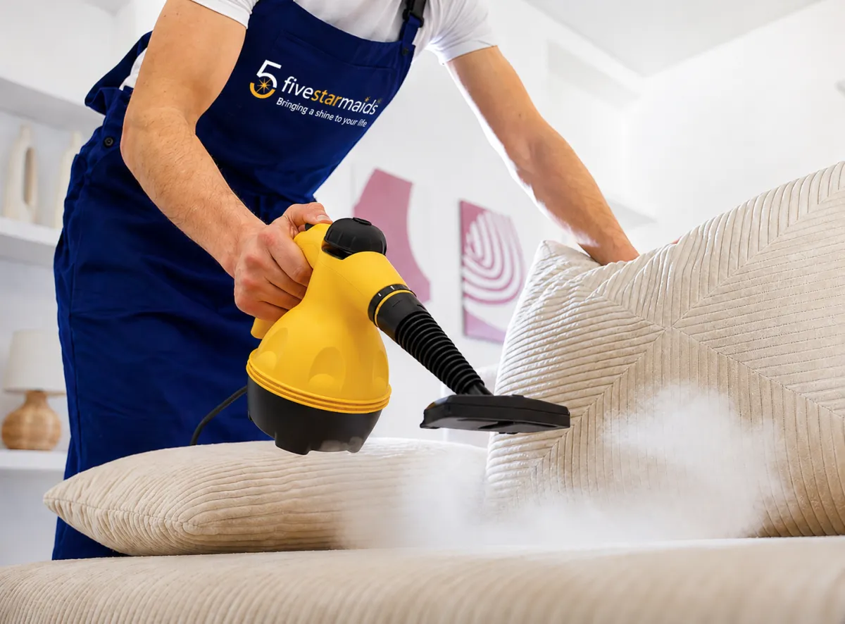 Professional home cleaner using steam cleaner on sofa cushions during residential upholstery cleaning service