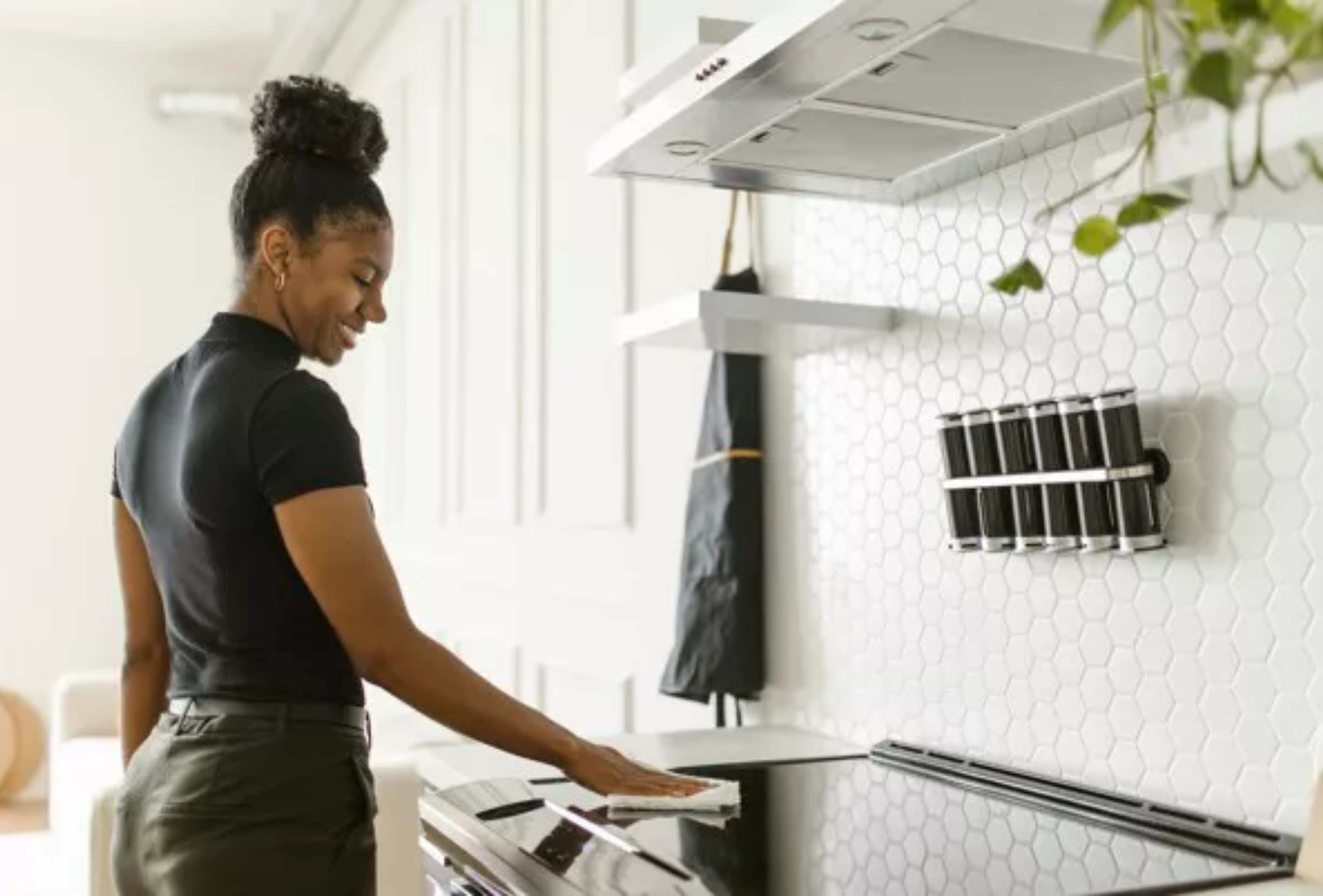 A person wiping kitchen stove as part of house cleaning services