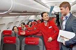 Flight attendant in red uniform smiling is showing a passenger  to his seat during training