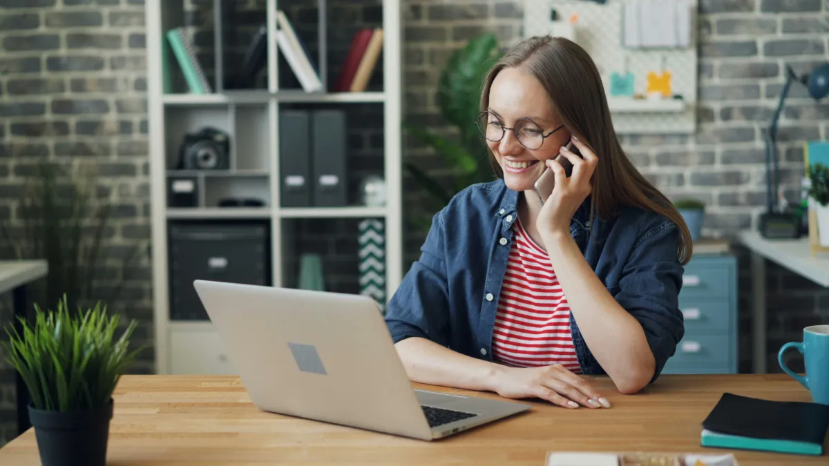 A woman talking on a cell phone with the 24/7 answering servicewhile using a laptop