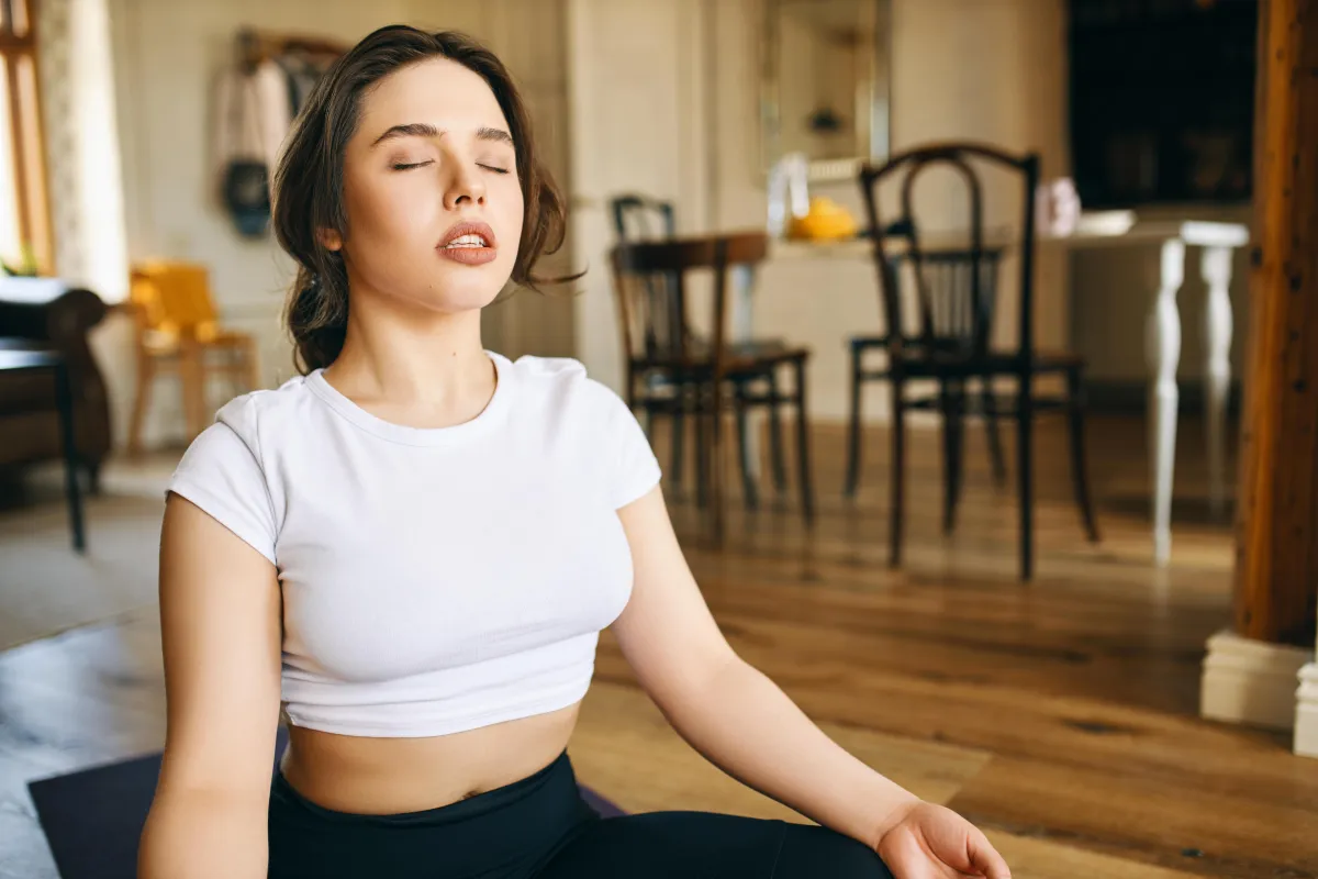 Calm woman breathing deeply in a sunlit room during energy healing session.