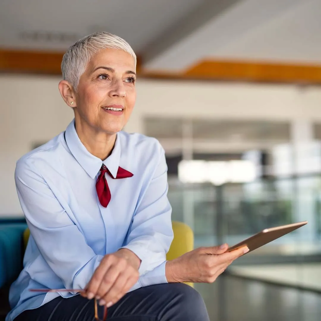 Smiling professional woman in office holding tablet, suggesting confidence and clarity in a work environment
