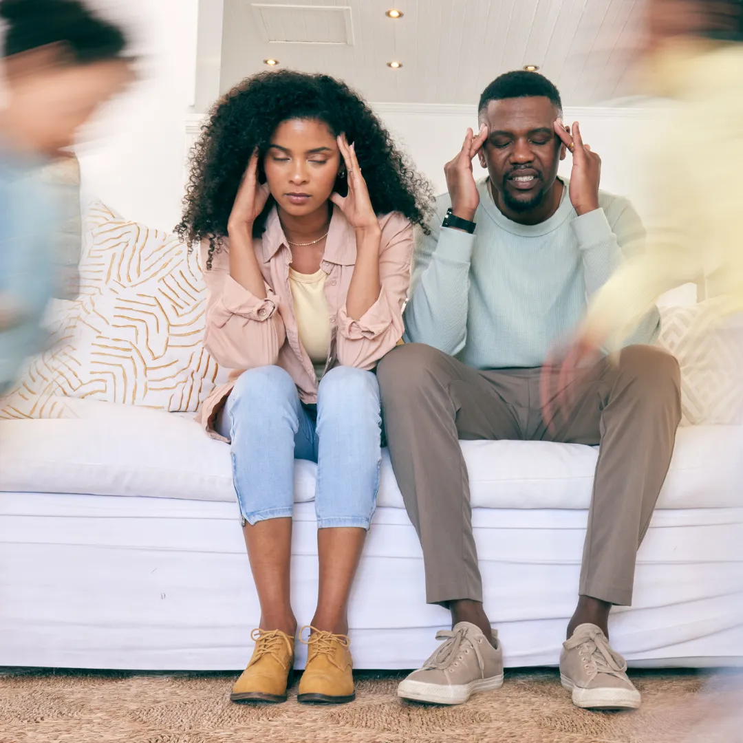 Frustrated parents sitting on a couch with hands on their heads while children blur past them, symbolizing overwhelm and tech-related parenting stress.