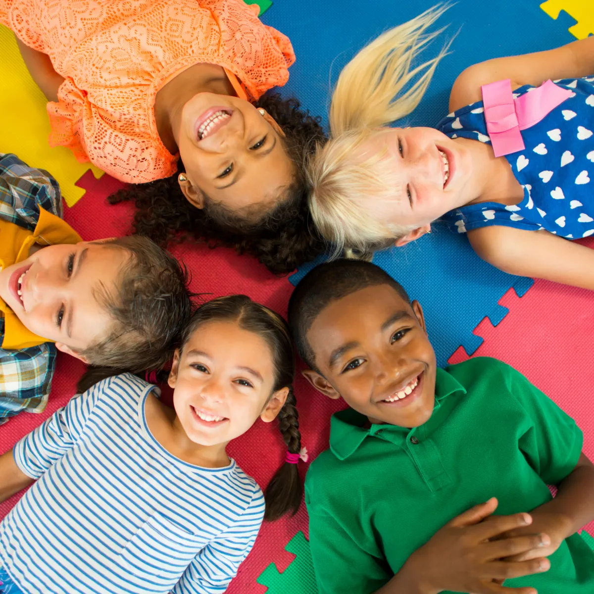Diverse group of happy children lying on colorful mats, symbolizing connection, joy, and a screen-free childhood.