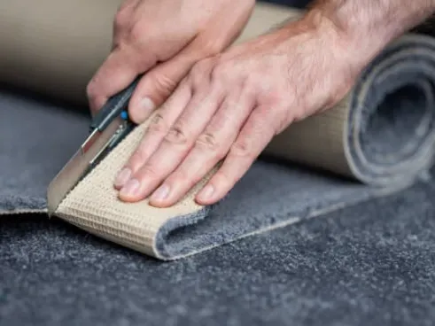 Close-up image of a man cutting a carpet edge with a stanley knife