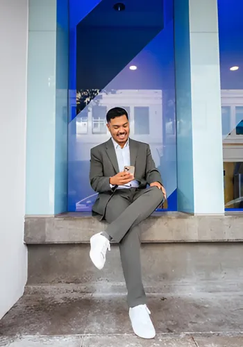 Shawn Gee sitting confidently in a gray suit, smiling and using a smartphone, representing professional real estate services in Baton Rouge.