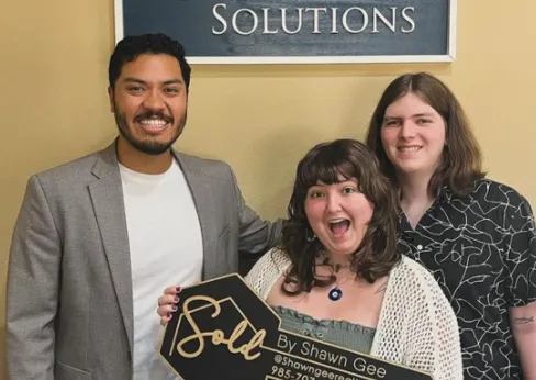 Shawn Gee posing with excited clients holding a 'Sold by Shawn Gee' key after helping them find their perfect home.