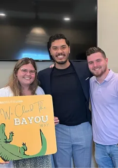 Shawn Gee smiling with a group of clients holding a custom 'Welcome to the Bayou' sign, celebrating their new property in Louisiana.