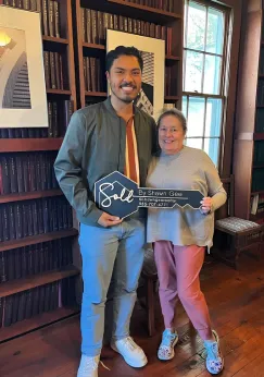 Shawn Gee standing in a cozy office with a client holding a 'Sold by Shawn Gee' key after a successful real estate purchase.