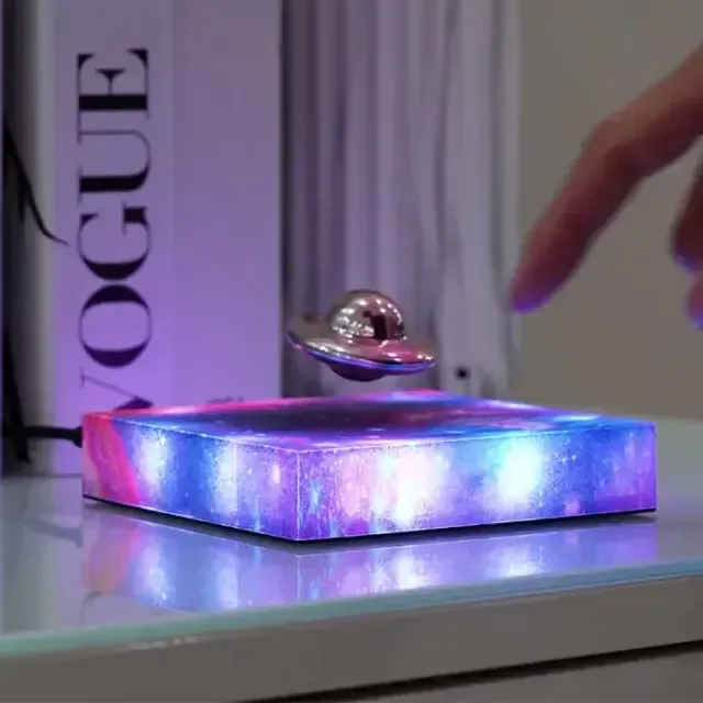 A levitating UFO-shaped galaxy lamp hovering over a magnetic base with glowing purple atmospheric lighting.